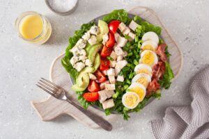 Cobb salad in bowl on wooden cutting board