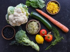 Cauliflower, broccoli, carrot, squash, corn, beans, tomatoes, and lemon on table