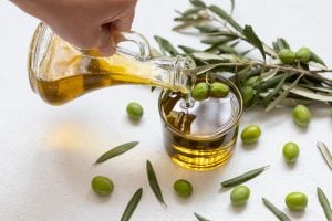 Raw olives on table and person pouring olive oil into glass carafe