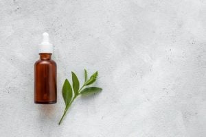 Tea tree essential oil bottle with dropper next to herb