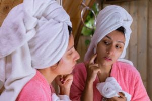 Woman with acne looks at reflection in mirror
