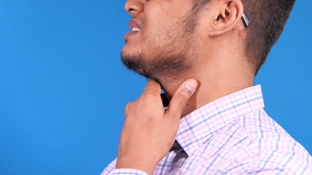 Man with glasses winces as he touches throat