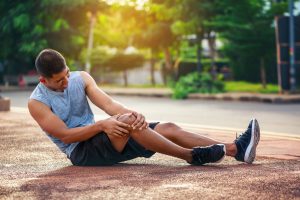 man with knee injury sits on road in pain