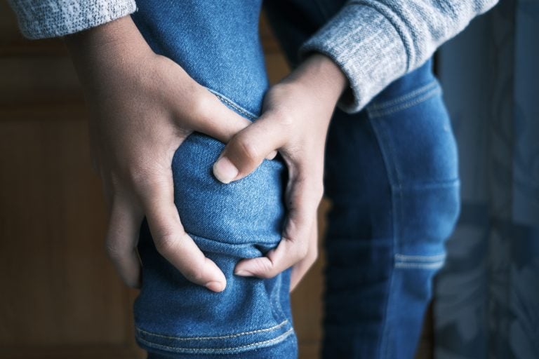 person wearing jeans holds knee in pain