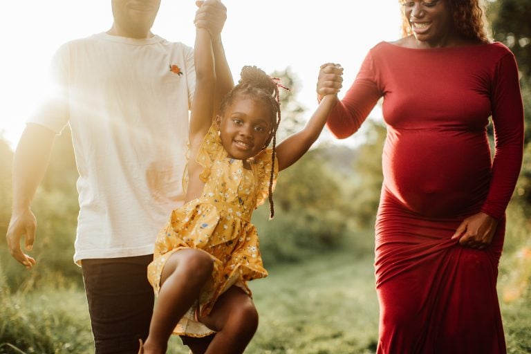 pregnant woman holds hands with man and daughter while walking outside