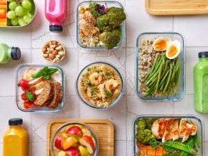various fruits, vegetables, whole-grain pasta, and proteins in glass containers on table