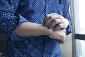 man in blue shirt scratches hand