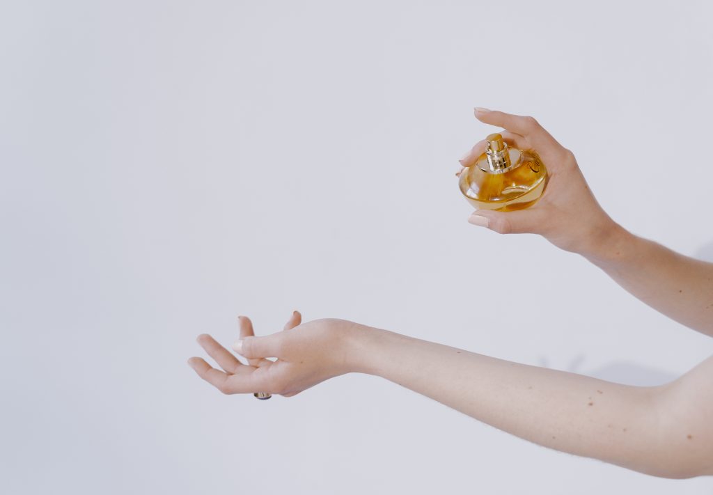 woman sprays wrist with perfume bottle