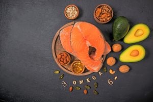 salmon, avocado, nuts, grains, and omega three capsules in bowls and scattered on table