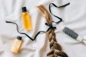 braided hair with ribbon next to bottles of hair product and brush