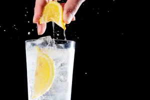 person squeezes lemon into glass of water with ice