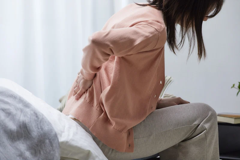 woman on bed touches lower back