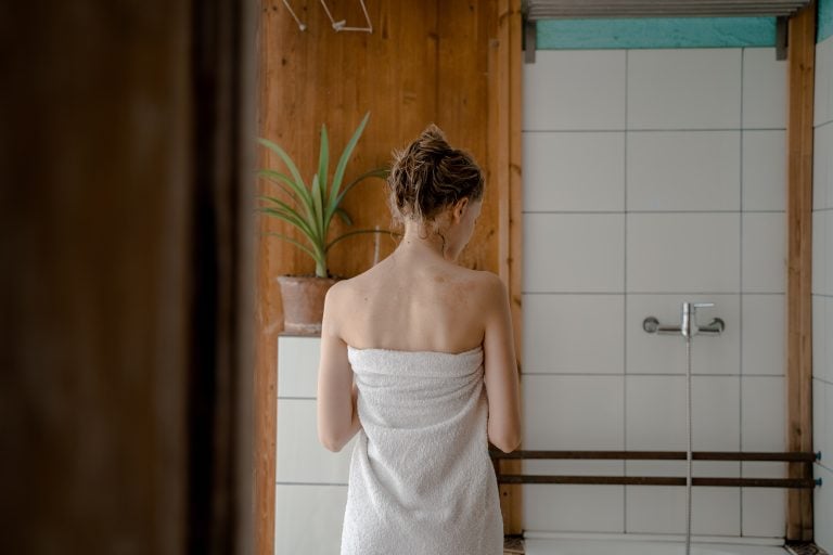 back of woman standing in bathroom wrapped in towel