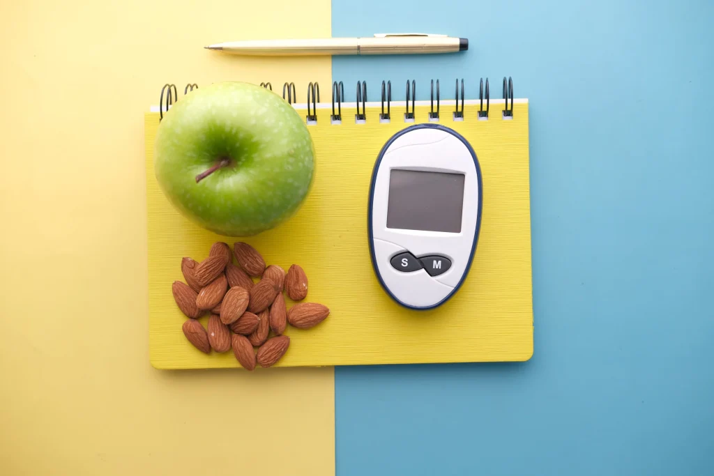 green apple and almonds on notebook beside blood sugar detection device