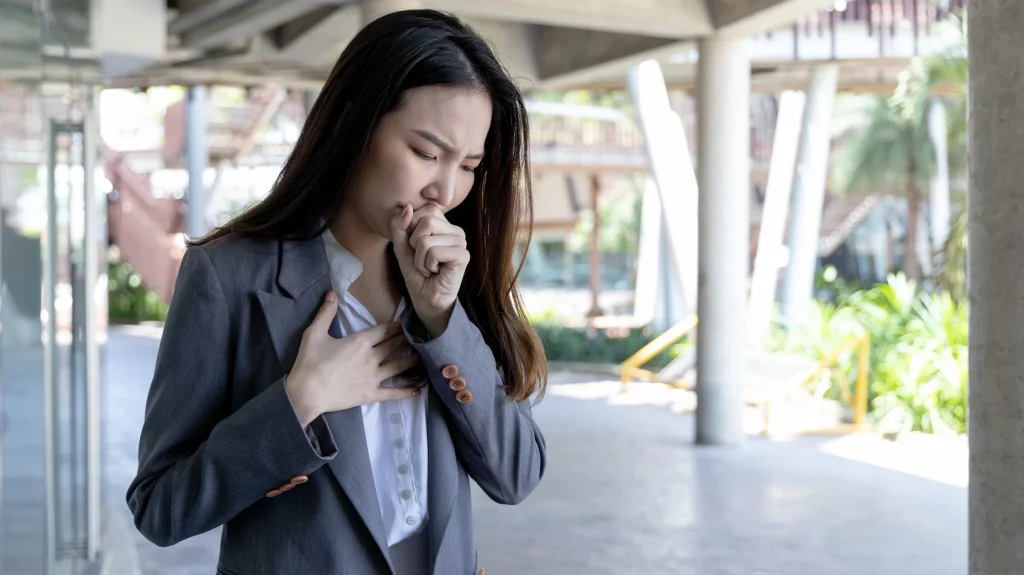 woman places hand over chest while coughing under building