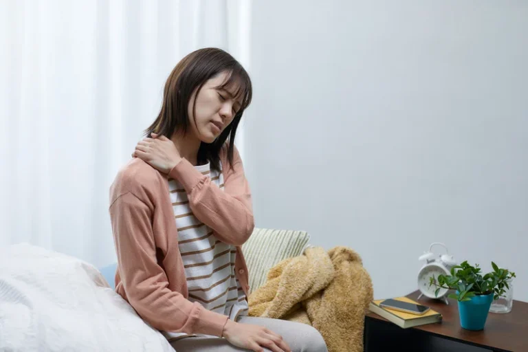 woman with pain touches neck on bed