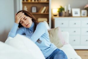 exhausted woman on couch places hand on forehead
