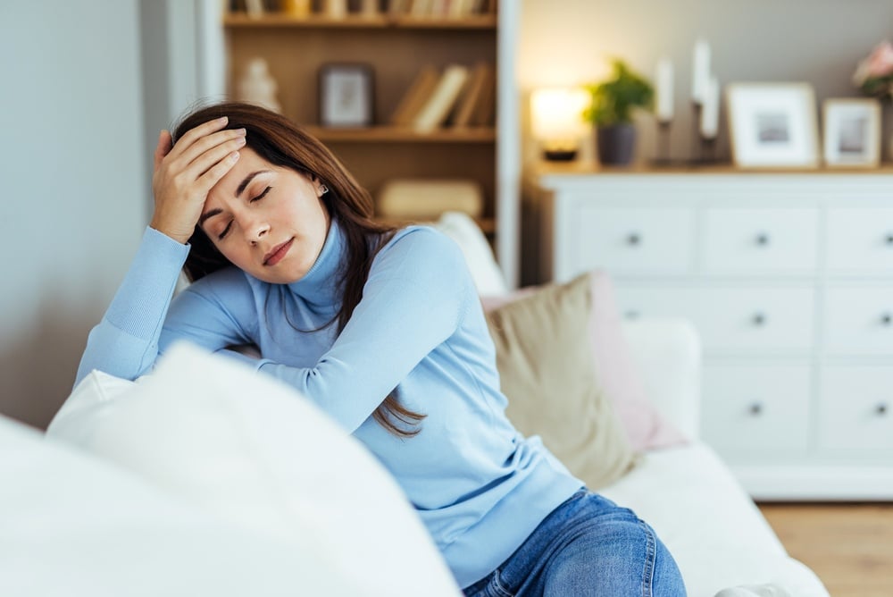 exhausted woman on couch places hand on forehead